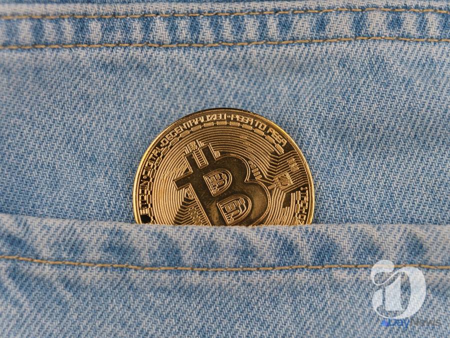 O monedă fizică de Bitcoin din aur ieșind dintr-un buzunar de blugi albaștri